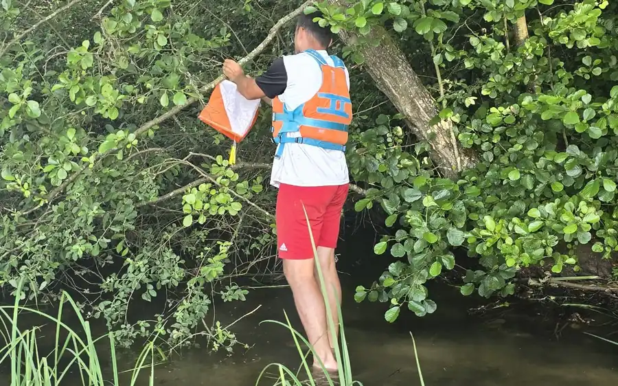 Un membre de l'équipe accroche une balise au-dessus d'un ruisseau, lors d'un parcours d'orientation